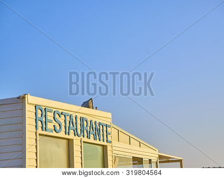 A White Beach Hut With A Blue Restaurante Sign.