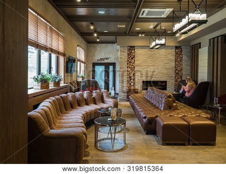 Hotel Lounge With Beautiful Sofas And Fireplace. A Woman Is Sitting In A Chair And Reading A Book. R