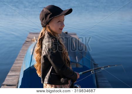 Child Is Fishing From Wooden Pier On A Lake. Cute Little Schoolgirl Have Fun Fishing. Leisure During