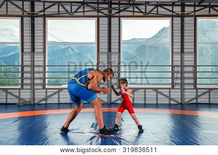 A Little Wrestler Boy In A Sports Tights Wrestles With An Adult Male Wrestler On A Wrestling Carpet 