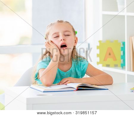 Cute sleepy bored school girl with opened mouth is dreaming at schooldesk