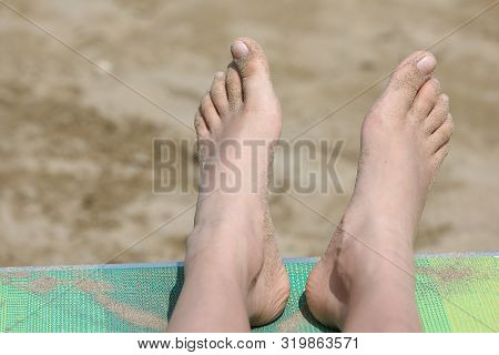 Two Feet Of A Girl On The Deck Chair On The Sandy Beach