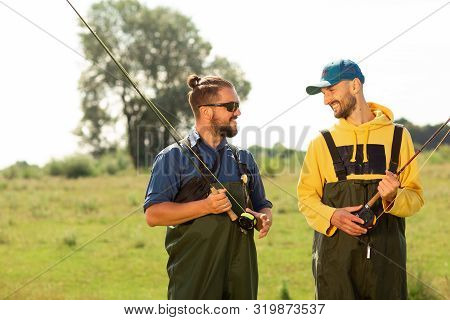 Two Fishermen Preparing For Fishing. They Hold The Fishing Rods And Talk To Each Other. Sport Fishin