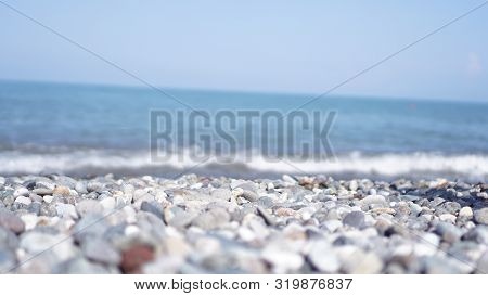 Pebble Stones On The Shore Close Up In The Blurry Light In The Distance Background.