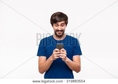 Handsome Brunet Man In A Blue Shirt With Beard And Mostaches Shocked Holding Smartphone Looking At T
