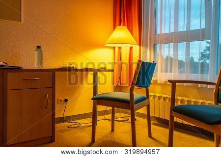 A Room Filled With Golden Light  From Yellow Floor Lamp With Two Blue Chairs And A Window With Orang