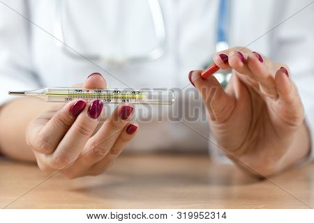 Doctor Holding In Hands A Red Pill And A Thermometer With High Temperature.