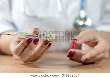 Doctor Holding In Hands A Red Pill And A Thermometer With High Temperature.