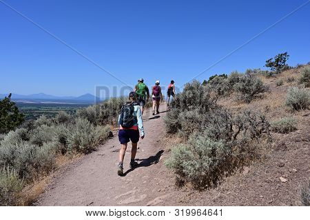 Hikers On Misery Ridge Trail In Smith Rock State Park Near Terrebonne, Oregon On A Cloudless Summer 