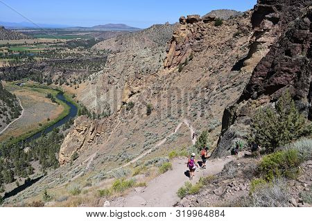 Hikers On Misery Ridge Trail In Smith Rock State Park Near Terrebonne, Oregon On A Cloudless Summer 