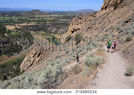 Hikers On Misery Ridge Trail In Smith Rock State Park Near Terrebonne, Oregon On A Cloudless Summer 