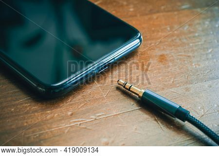 Headphone Cable Lying In Front Of A Smartphone Without Headphone Jack On Wooden Table