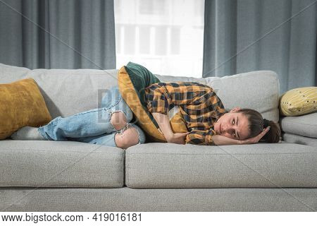 Young Woman With Menstruation Is Lying Down On The Couch And Holding On To Her Stomach Because She I