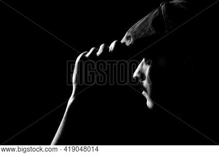 Black And White Portrait Of A Young Guy With Moustache Holding His Hat On Black, Dark Background.