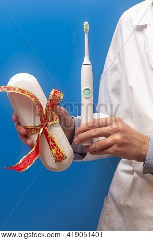 A Guy In A White Coat Holds A White Electric Toothbrush In His Hands. Gift Set. Dental Hygiene. Red