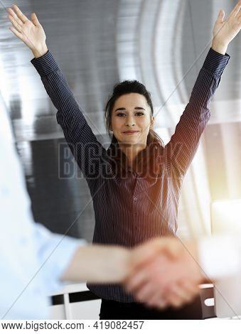 Happy And Excited Business Woman Raising Hands Because Of Success Agreement At Meeting. Two Men Shak