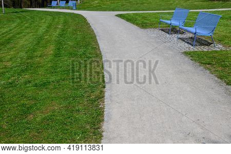 Park Benches In Light Blue Made Of Metal Strips Similar To A Lattice. Trash Can And Beautiful Lawn W