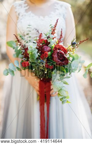 A Bride In A Pale Gray Wedding Dress Holds A Bouquet With Red Peonies, Astilba, Roses And Eringium A