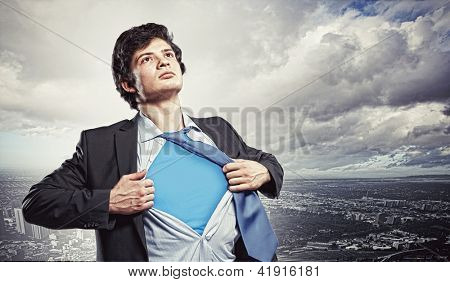 Immagine di giovane imprenditore mostrando supereroe vestito sotto i suoi piedi camicia contro città backgro