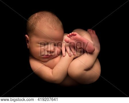 7 days old baby boy posed in the curled up pose of an unborn foetus