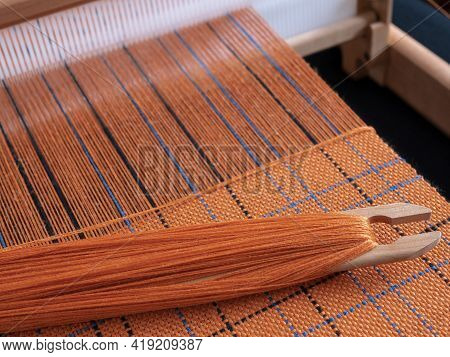 Wooden Loom With Shuttle And Woven Orange Textile With Striped Pattern. Concept Of Handloom Weaving