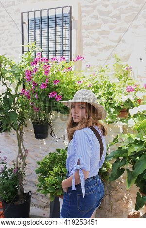 A Girl In A Straw Hat Walks Along A Narrow Street With Many Flowers In Flower Pots Along The White W