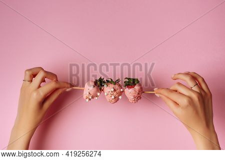 A Girl Holds Strawberries Covered In Chocolate On A Pink Background
