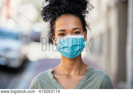 Portrait of happy african woman looking at camera with surgical mask due to covid-19. Close up face of beautiful black girl wearing protective face mask against the spread of coronavirus disease.