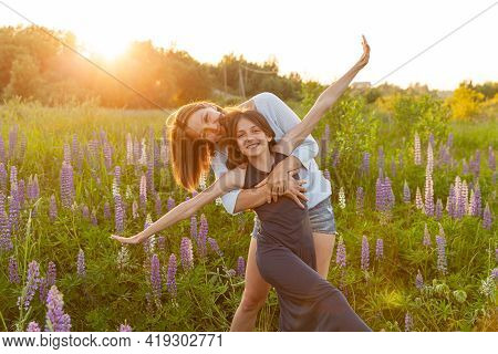Young Mother Embracing Her Child Outdoor. Woman And Teenage Girl On Summer Field With Blooming Wild 