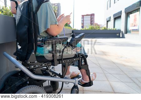 Disabled Handicapped Woman In Wheelchair Using Smartphone And Smiling At Camera While Walking Outdoo
