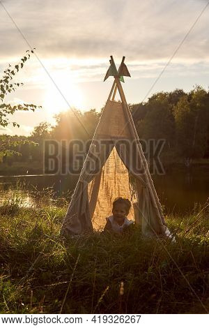 A Little Girl Is Sitting By The Lake. Sunny Akat. Wigwam. Happy Child.