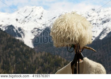 A Mountain Hat Made Of White Sheep Wool And A Fragment Of A Felt Cape On The Background Of Mountains