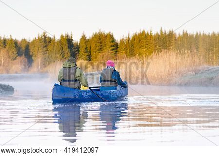 Retirees Rowing A Canoe In Early Spring In The Early Morning. Seniors Lifestyle. Morning Landscape, 