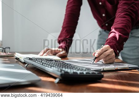 Asian Man Programmer Holding Pen To Writing Code Data On Document In Clipboard While Working To Rech