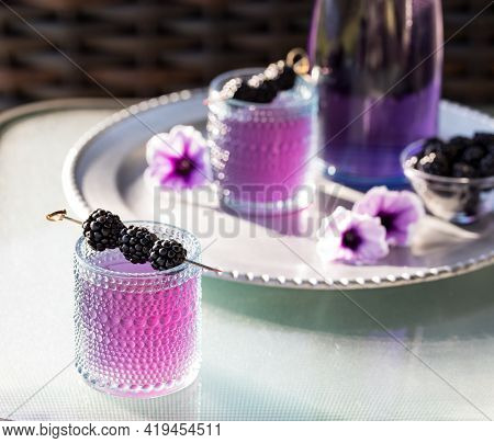 Blackberry Mocktail With Blackberry Skewer And A Tray Of The Same In Soft Focus In Behind.