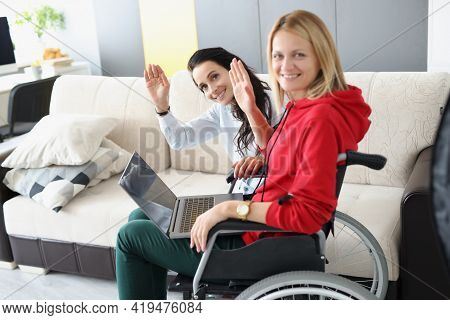 Woman In Wheelchair With Laptop On Her Legs And Her Friend Waving Her Hand In Gratitude