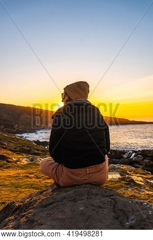 A Young Woman Relaxed At Sunset In The Cove Of Stones In The Jaizkibel Mountain In The Town Of Pasaj