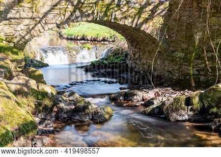 Long Exposure Of The Weir Water  River Flowing Under Robbers Bridge In Exmoor National Park
