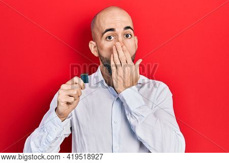 Young bald man holding sdxc card covering mouth with hand, shocked and afraid for mistake. surprised expression 