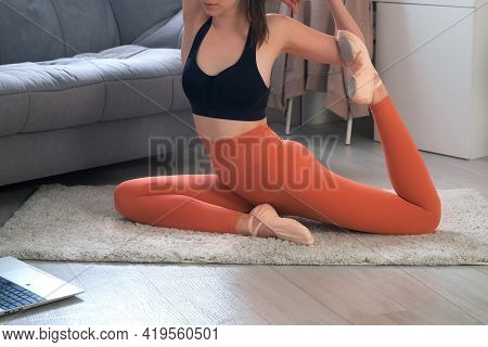 Young Woman Is Practicing Yoga Doing Pigeon Pose At Home Online Training With Laptop. She Is Stretch