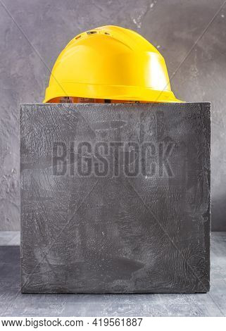 Construction hard hat at concrete cube or blocks near wall background texture. Yellow helmet and concept of minimalism design