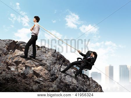 Imagem de dois jovens empresários, puxando a corda no topo da montanha contra o fundo da cidade