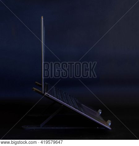 The Slim Modern Laptop Or Ultrabook Sits On A Portable Holder Against A Dark Background. Side View. 