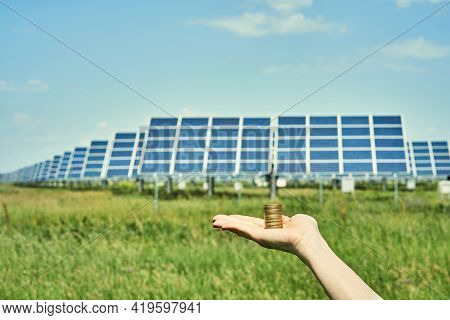 Hand holding money banknote with photovoltaic solar energy panels in background,
