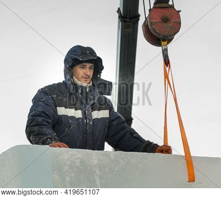 A Portrait Of A Fitter In A Blue Jacket At The Hook Of A Truck Crane