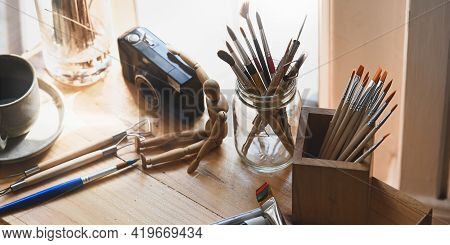 Paint Brush In Glass Vase Putting On Wooden Working Desk That Surrounded By Camera, Wooden Puppet, P