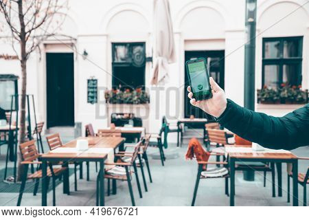 Vaccinated person using immunization certificate on smartphone at the restaurant or terrace. 