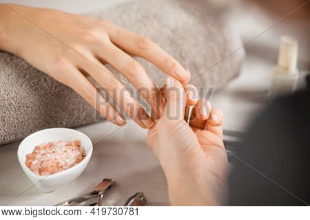 Close up of beautician hands doing hand treatment at nail salon. Woman holding the finger of customer during manicure. Detail of hands of manicurist massaging client fingers in manicure salon.