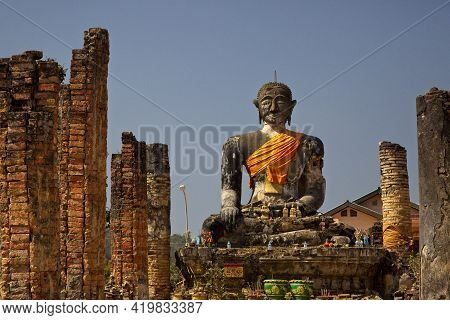 Huge Stone Statute Of Buddha Looking Forward Wrapped In Orange Clock Monastry Phonsavan, Laos.