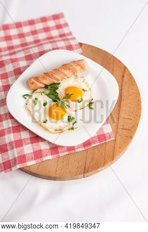 2 Fried Eggs And Fried Sausage Garnished With Parsley On A White Plate